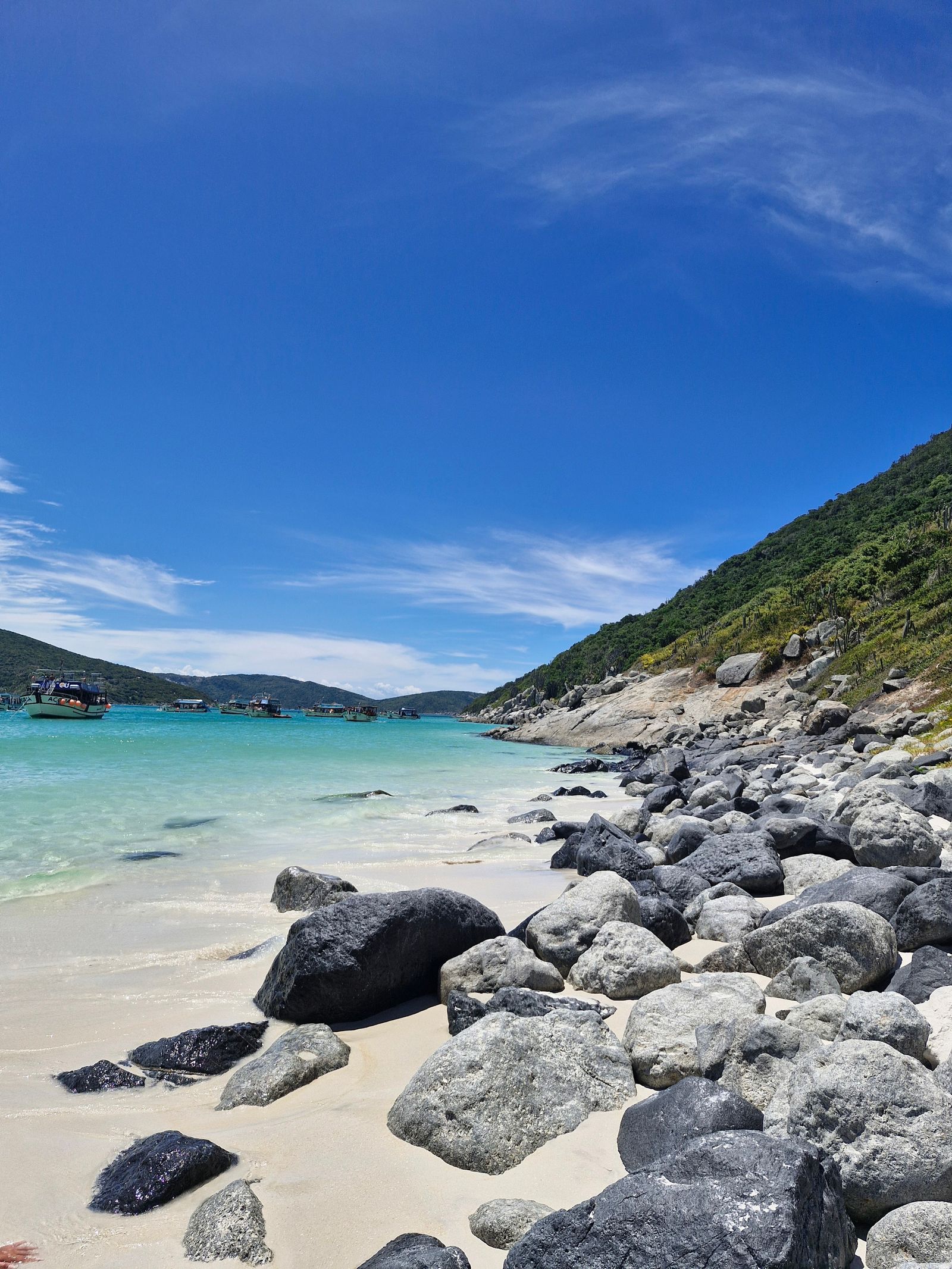 Praia de Arraial do Cabo com água azul-turquesa, faixa de areia e costões.